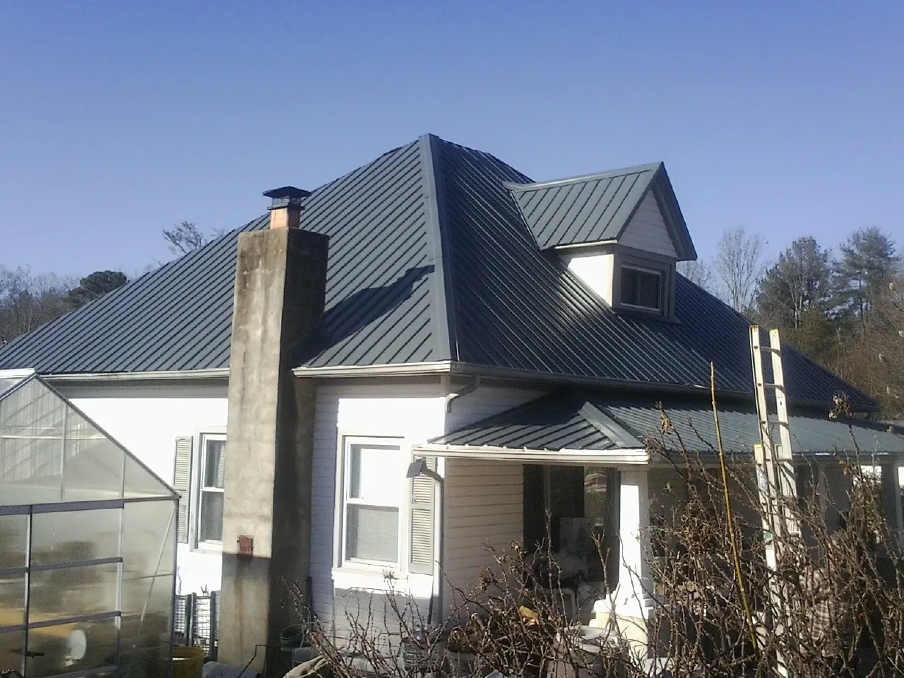 Dark blue standing seam metal roof on a white farmhouse with dormer — Slate & Tile Roof Repair by Roofing Brothers in Calhan