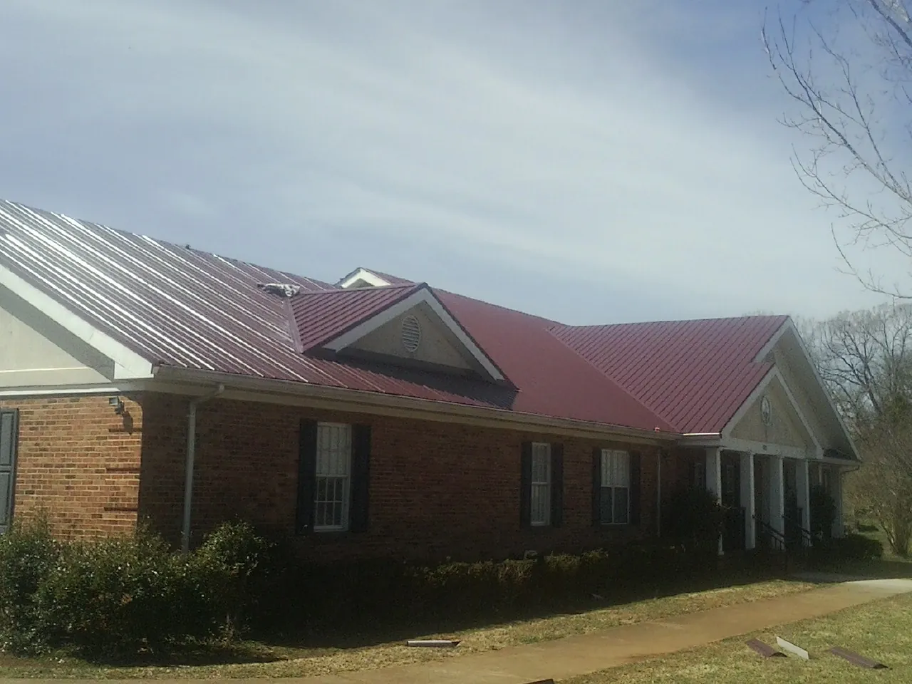 Red metal roof with gabled entries on a long brick building, from a Hail Damage Roof Repair job in Calhan