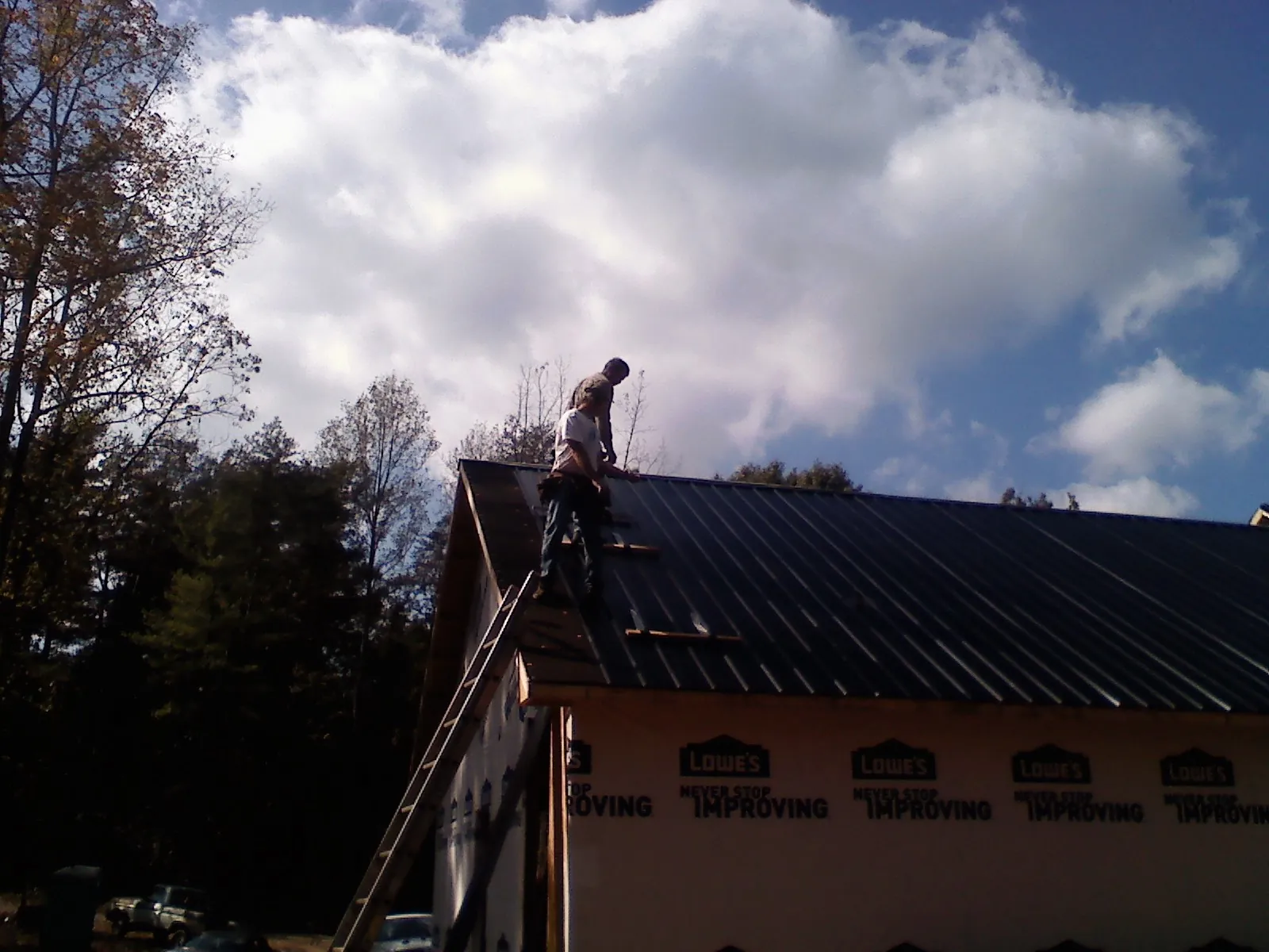 Roofer fastening dark metal panels high against a cloudy sky, from a Roof Inspection job in Calhan