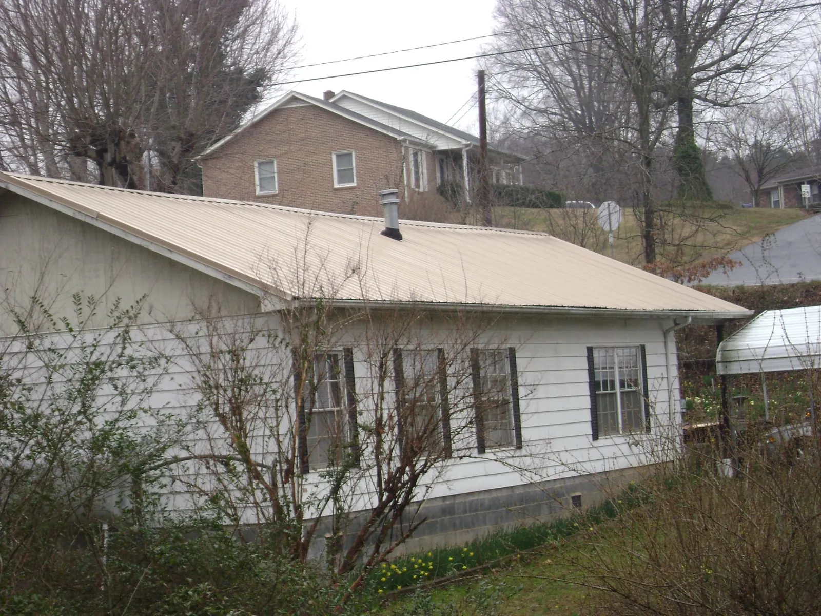 Tan metal roof on a white sided house set into a hillside — Commercial Roofing by Roofing Brothers in Calhan