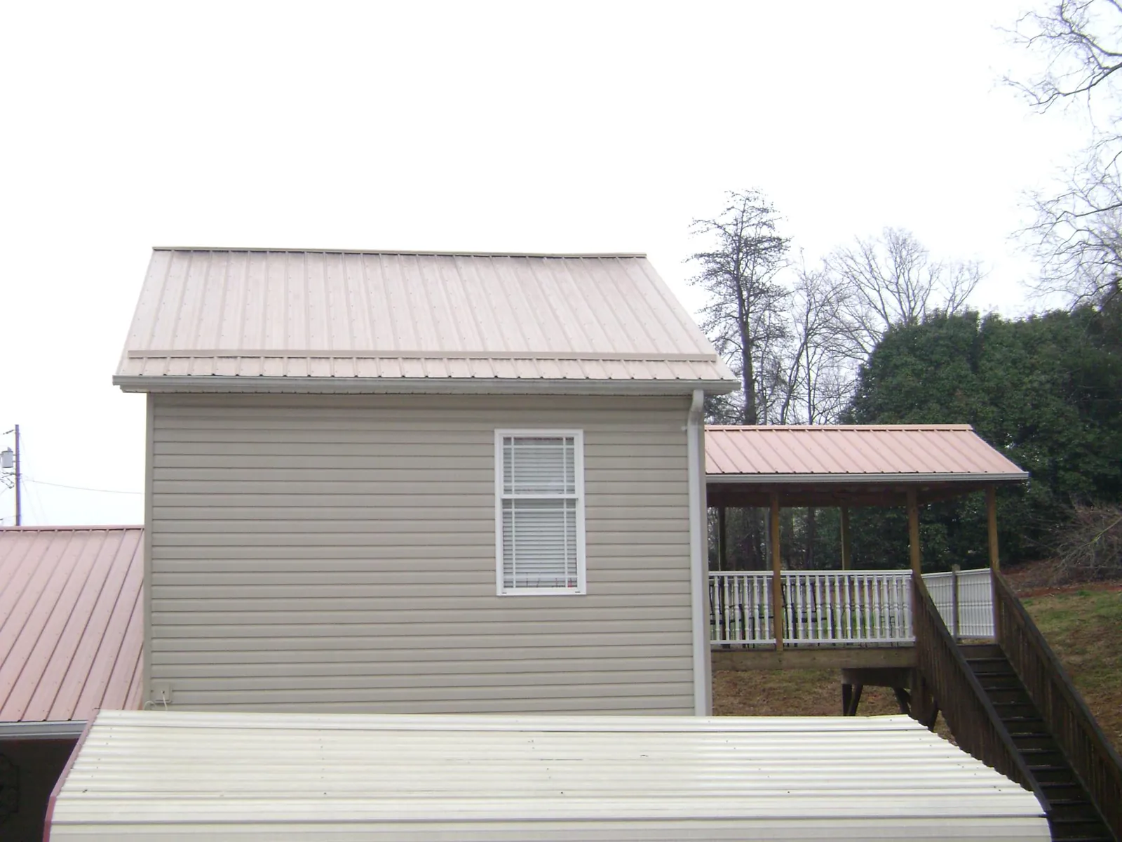 Tan metal roofs on a two story addition and attached porch, from a Roof Replacement job in Calhan
